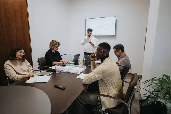 A diverse group of colleagues collaborating in a boardroom meeting, analyzing statistics and strategizing for business growth and profitability.
