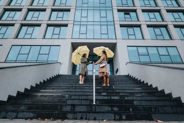 Uprostřed Městského Pozadí Dvě Stylové Ženy Konverzují Schodech Žlutými Deštníky — Stock fotografie