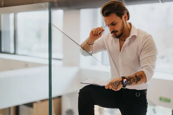 Fokuserad Ung Manlig Entreprenör Med Tatueringar Djupt Överväger Samtidigt Läsa — Stockfoto