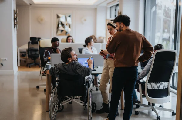 一个现代化的办公室场景描绘了一个充满活力的团队 其中包括坐在轮椅上的专业人士 他们在一个明亮的工作空间中讨论各种想法并进行合作 — 图库照片