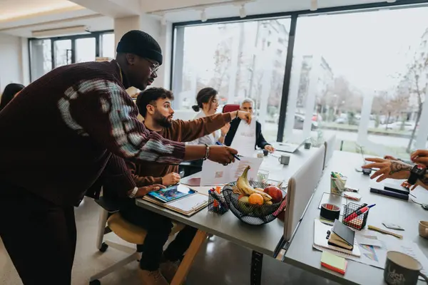 デジタルデバイスと健康的な軽食を備えた近代的なオフィステーブル周辺のビジネス戦略を共同で議論する多様な専門家のグループ — ストック写真