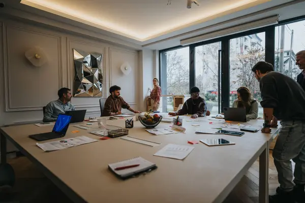 A multiethnic team engages in a business meeting in a well-lit, contemporary office. The image captures teamwork, discussion, and planning.