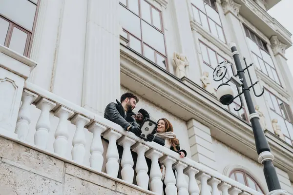 A group of three young adults bonding on an ornate balcony, sharing a conversation with a scenic urban background.