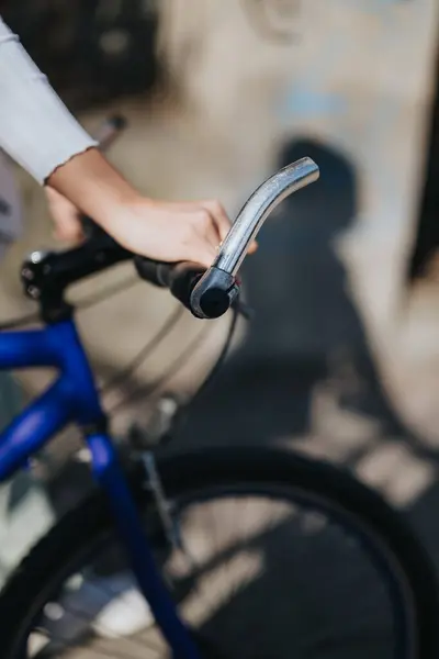 A detailed view of a person holding the handlebar of a classic blue bike, evoking urban mobility and lifestyle.