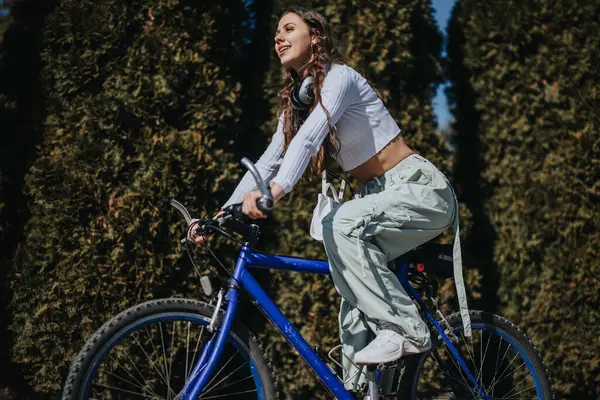 一个年轻活跃的女人 带着耳机骑自行车 在阳光明媚的天气里享受户外活动 — 图库照片