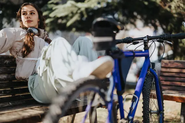 一位心事重重的年轻女子躺在长椅上 在阳光灿烂的公园里骑着自行车 流露出一种悠闲宁静的感觉 — 图库照片