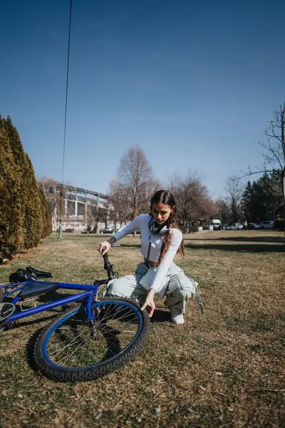 Una Joven Está Arrodillada Junto Bicicleta Azul Examinándola Mientras Disfruta —  Fotos de Stock