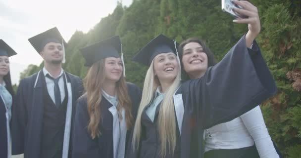 Graduados Felices Vestidos Con Gorras Vestidos Toman Selfie Alegre Parque — Vídeo de stock