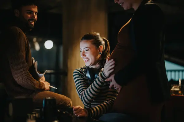 Young, beautiful, business partner working late at night in modern office setting. Beautiful woman touching her pregnant partners stomach and smiling after she felt the babys kick.