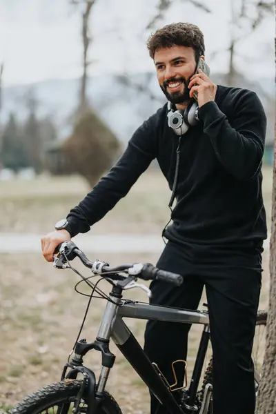 笑顔の若い大人の男性は屋外活動を楽しんで 彼の自転車に乗って自然な設定で電話で追いつく — ストック写真