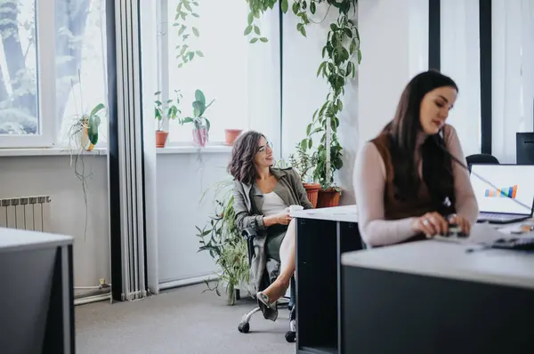 两名职业女性在一间室内植物明亮的办公室里工作 其中一人专注于向同事微笑 — 图库照片