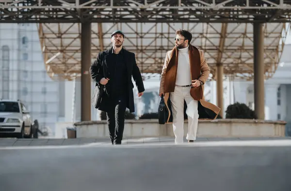 Urban elegance and business style underscore this image of two fashionable men carrying bags, evoking themes of commuting, work, and city life.