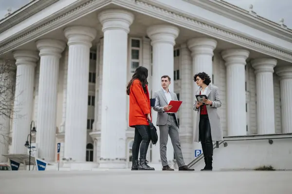 Three lawyers engage in a professional meeting outside a classic courthouse, collaborating on legal documents.