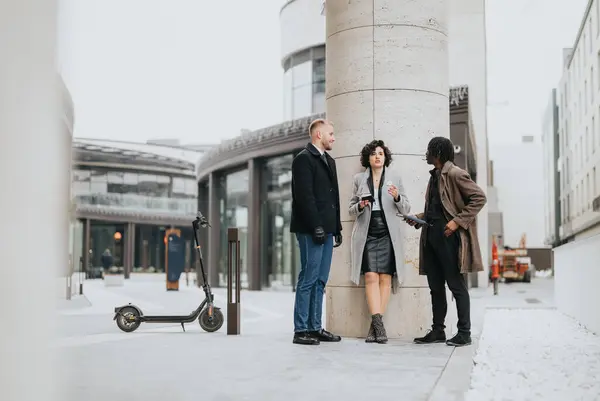Three business people engage in a conversation on a city street with an electric scooter nearby, showcasing a modern urban meeting.