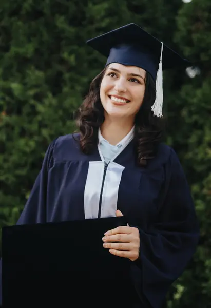 幸せな女性の卒業生は公園で彼女の学位を祝い 彼女のキャップを保持し 彼女の大学の成功の肯定的な思い出とポーズ — ストック写真