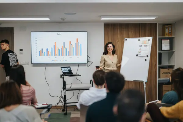 自信的女性专业人员在屏幕上向全神贯注的办公室观众展示销售图表 传达成功和团队合作的信息 — 图库照片