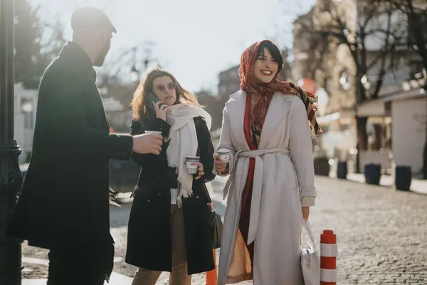 友人のグループは街で晴れた日を楽しんでおり コーヒーカップで通りを歩き チャットして一緒に笑っている — ストック写真