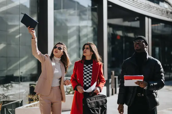タブレットと文書を持つ3人の若い多民族専門家が 現代のオフィスビルの外で歩き 議論しています — ストック写真
