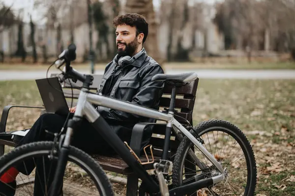Stylish businessman enjoys remote work in a park setting with his bicycle beside him, exemplifying a flexible modern lifestyle.