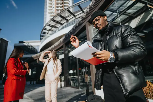 黒人のビジネスプロフェッショナルが書類を分析し 2人の同僚が都会の建物の外で会話する — ストック写真