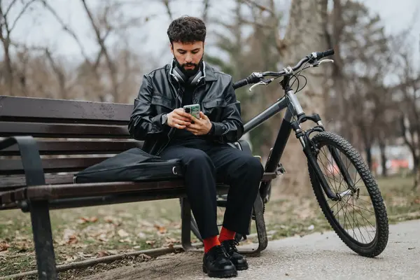 カジュアルな服装のハンサムなビジネスマンは 都市公園の設定で自転車で座っている間 遠隔で電話で動作します — ストック写真