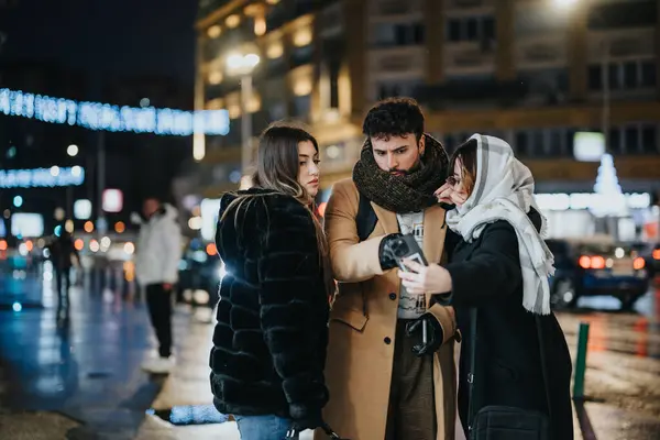 Young adults gather around a smart phone on a city street at night, engaged and collaborating in an urban environment.