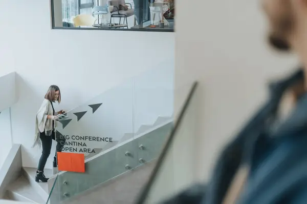 Businesswoman walking up office stairs and holding smart phone.