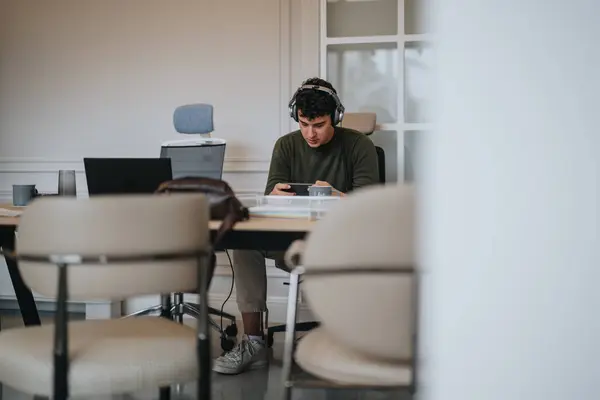 Skoncentrowany Młody Dorosły Słuchawkami Pracującymi Laptopie Jasnej Współczesnej Przestrzeni Roboczej — Zdjęcie stockowe
