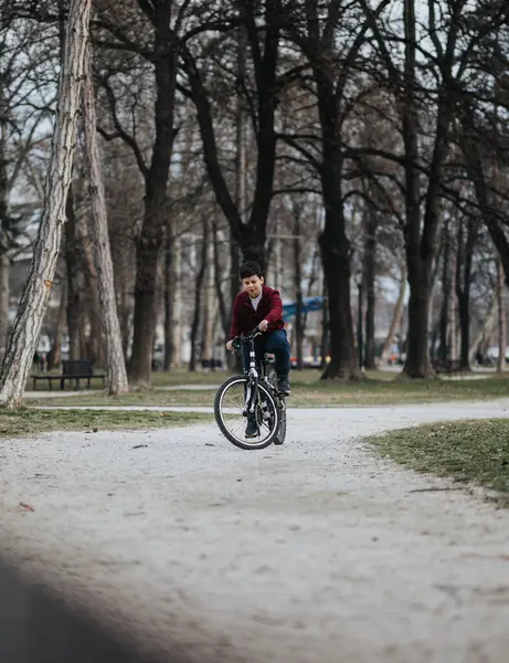 一个男孩骑着自行车悠闲自在地走在城市公园的一条小径上 周围环绕着自然和绿叶 — 图库照片