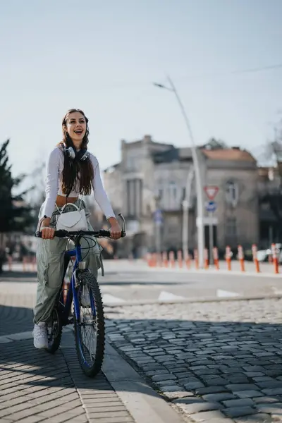 Веселая Молодая Женщина Наушниками Шее Ездит Велосипеде Городской Улице Демонстрируя — стоковое фото