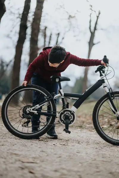专注的年轻骑车人在公园的小径上固定自行车轮 体现了健康 积极的生活方式 — 图库照片