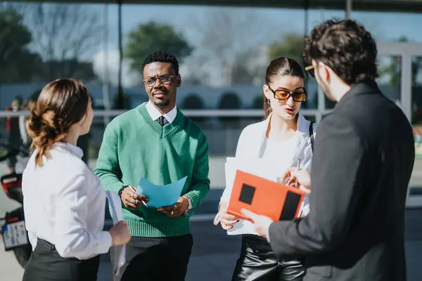A diverse group of businesspeople engage in a meeting outdoors with papers in hand, highlighting teamwork and collaboration in a sunny urban setting.