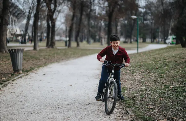 在一个繁茂的城市公园里 一个骑自行车的小男孩在一条小径上嬉笑 代表着童年的快乐和自由 — 图库照片