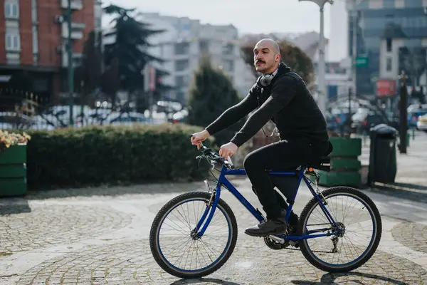 都会の通りをサイクリングする現代の大人の男性の側面 首の周りにヘッドフォン — ストック写真