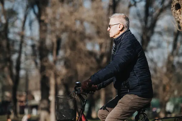 An elderly gentleman cycles through a park filled with trees, depicting activity, health, and enjoying life in older age.