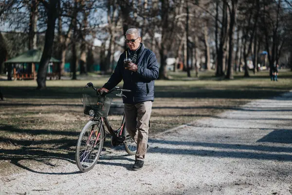 Active senior man with bicycle and coffee in a tranquil park setting.