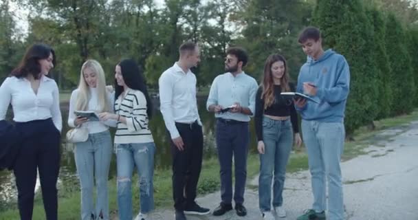 スマートフォンやタブレットを屋外で使用し 自然公園の環境でテクノロジーの使用と接続を体現する若々しいジェンダーグループ — ストック動画