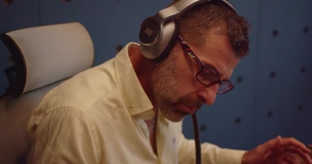 ヘッドフォンを使用して上級男性ビジネスリーダー 音楽を聴き オフィスのノートパソコンで作業しながら微妙な動きでダンスを楽しんでいます — ストック動画