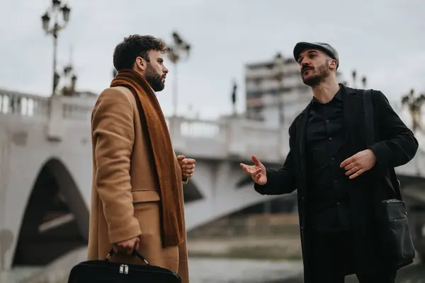 在一个背景为桥梁的城市里 拍摄到两名身着职业装的男子正在进行严肃的讨论的镜头 — 图库照片