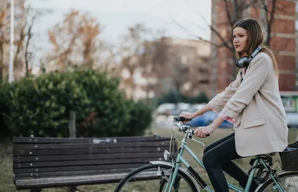 一位活跃的年轻女性带着耳机 晚上在一个宁静的公园里悠闲自在地骑自行车 — 图库照片