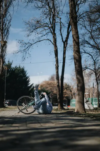 女性が静かな公園のセッティングで彼女の自転車から落ちて 裸の木と澄んだ空に囲まれた瞬間を撮影 — ストック写真