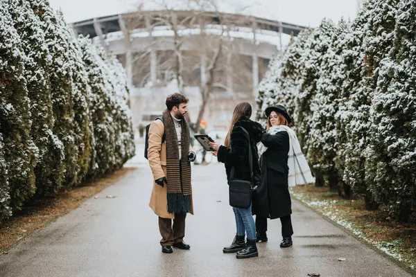 Two women embrace in a heartfelt reunion while a man looks on, set against a backdrop of snow-dusted trees on a chilly winter day.