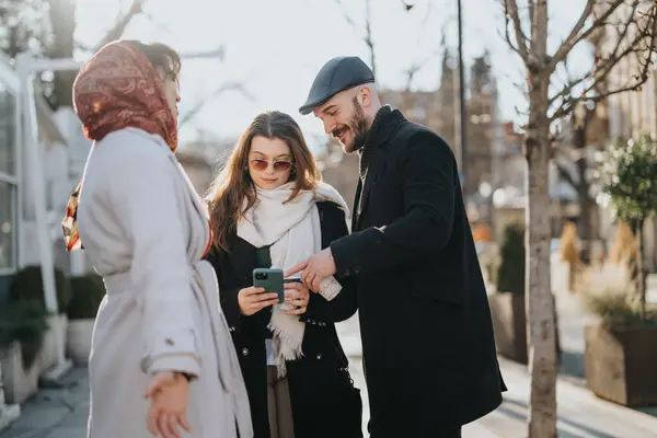 A joyful moment as three friends, two women and a man, engage with content on a smart phone on a sunny city street.