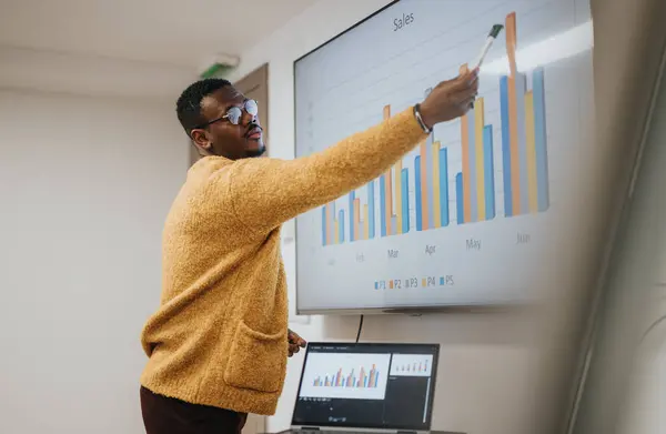 明るいオフィスの設定でホワイトボード上のチャートでプレゼンテーションをする自信のあるアフリカ系アメリカ人のビジネスマン — ストック写真