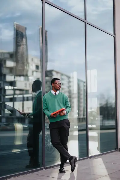 スマートな服を着た若い男性のプロフェッショナルは 都会の環境でガラスのファサードと一緒にタブレットを自信を持って歩きます — ストック写真