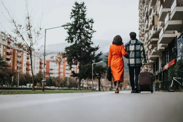A business couple in smart attire engaged in conversation while walking on a city street on an overcast day, exemplifying dynamic business life.