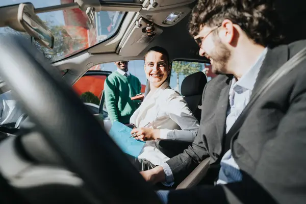 Two cheerful business professionals engaging in a conversation inside a car, commuting with a bright smile on a sunny day.