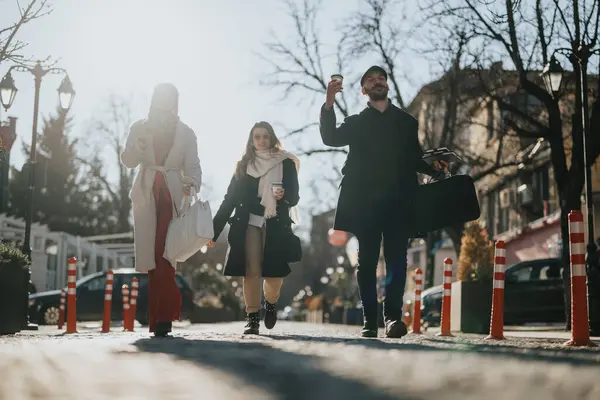 三个年轻人享受着城市的阳光 带着购物袋和咖啡散步 体现了城市生活 休闲和友谊 — 图库照片