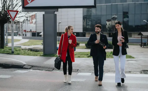 Three modern professionals in smart casual attire walking outside on a bright sunny day near a business center.