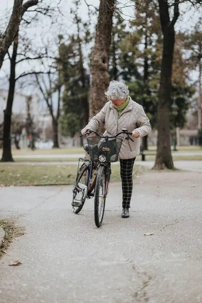 Active senior woman walking with her bicycle along a park pathway, embracing a healthy lifestyle in retirement.